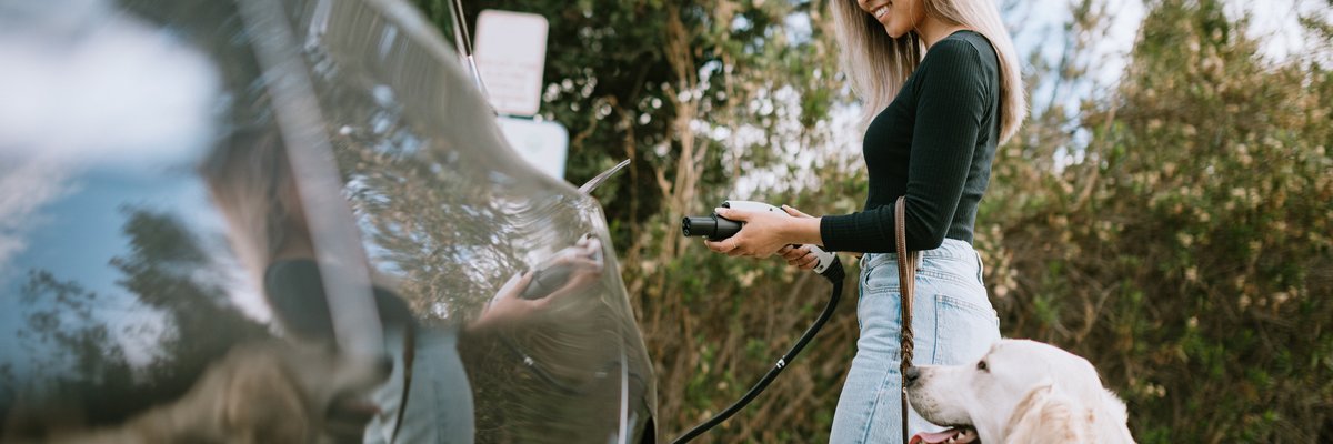 Woman with dog about to charge her electric car.