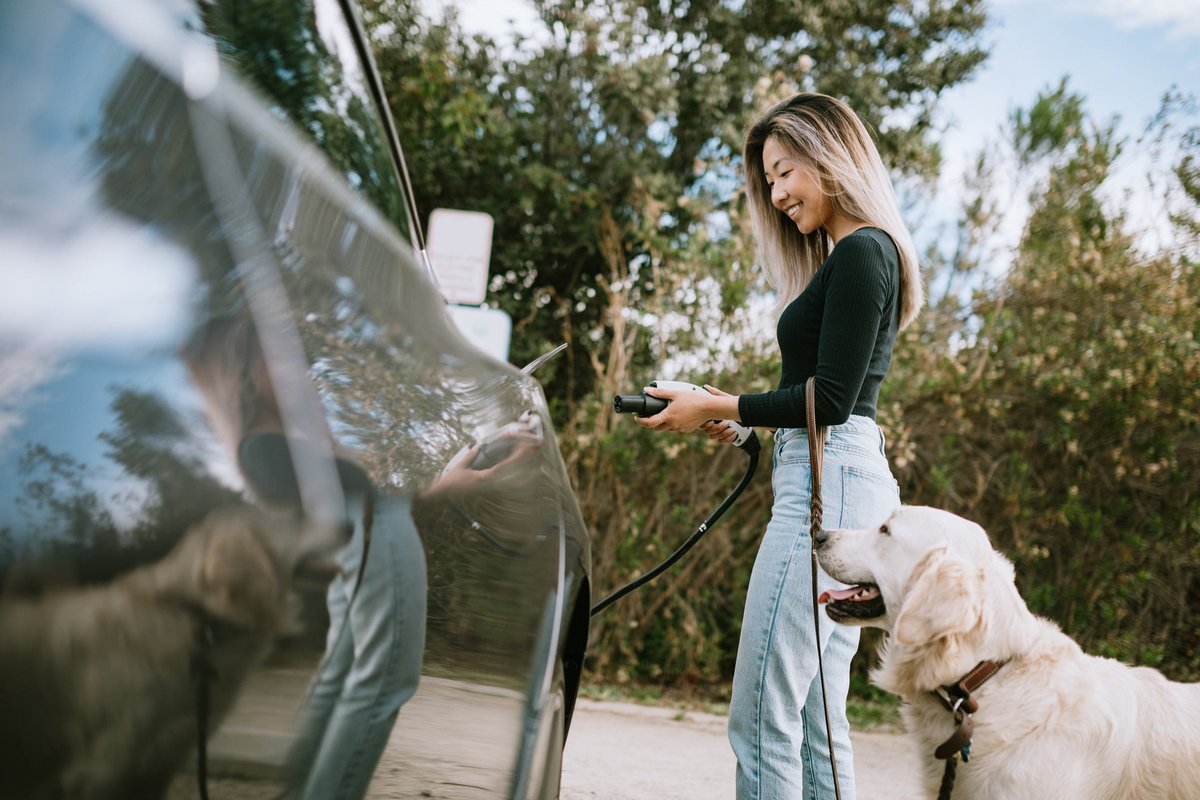 Woman with dog about to charge her electric car.