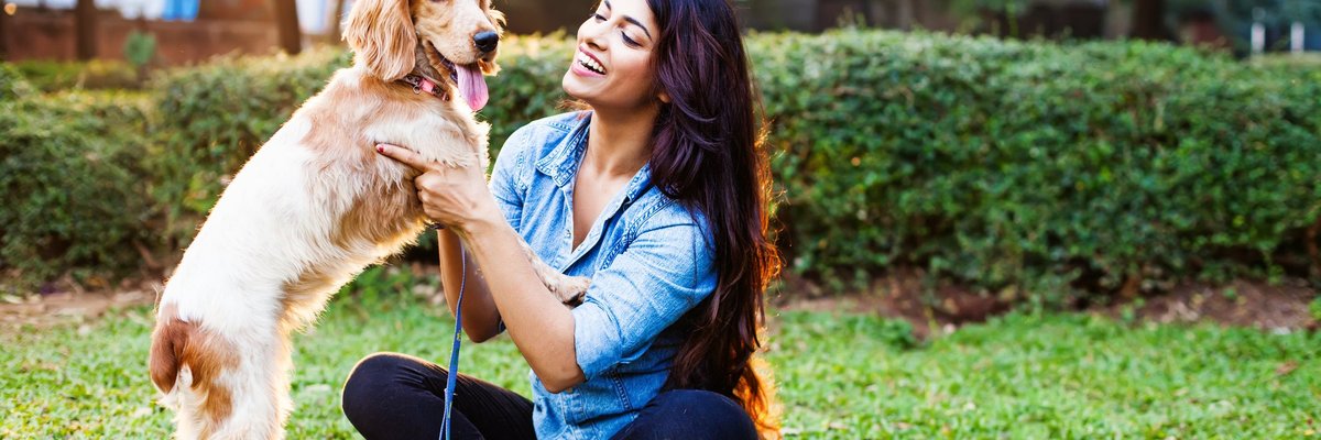 A woman sitting in a sunny park with a dog.