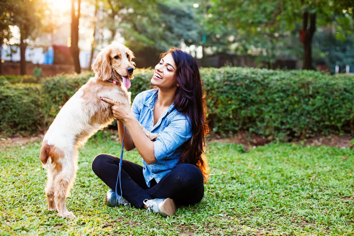 A woman sitting in a sunny park with a dog.