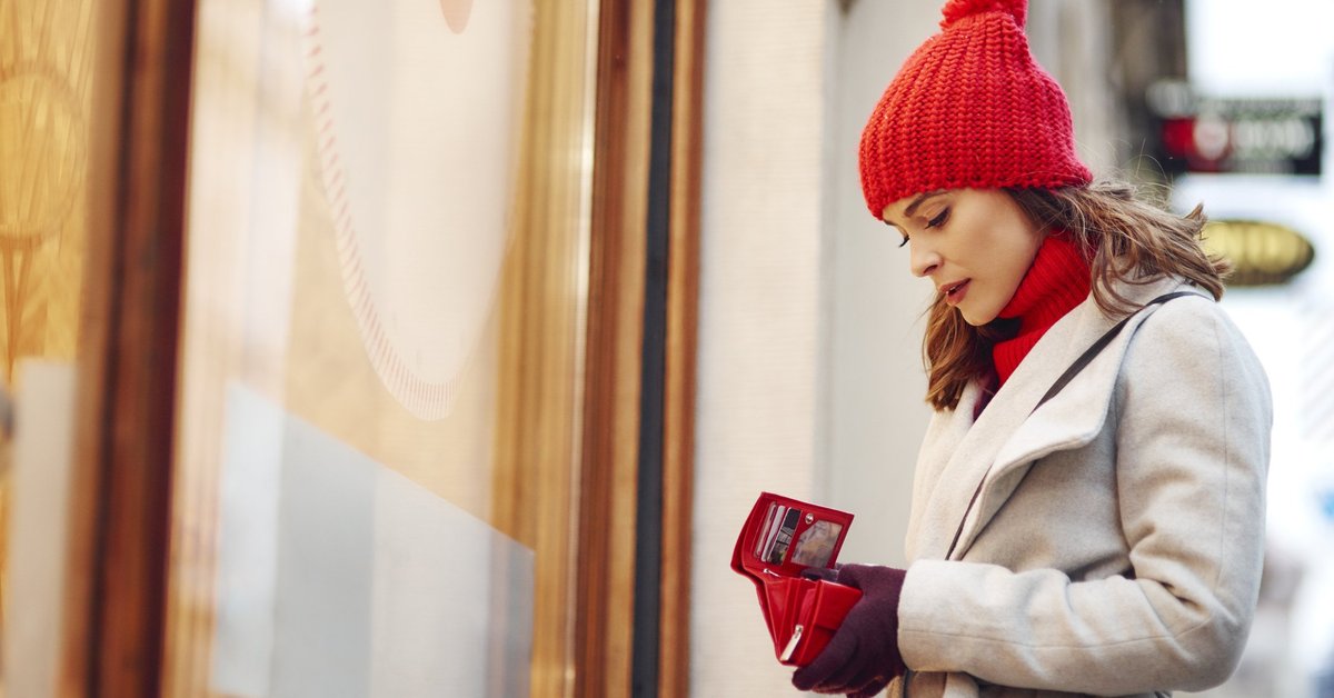  woman outside of a store looking into her empty wallet.