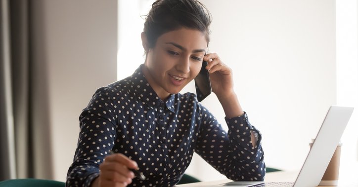 A young woman with a laptop and papers talking on the phone.