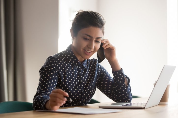 A young woman with a laptop and papers talking on the phone.