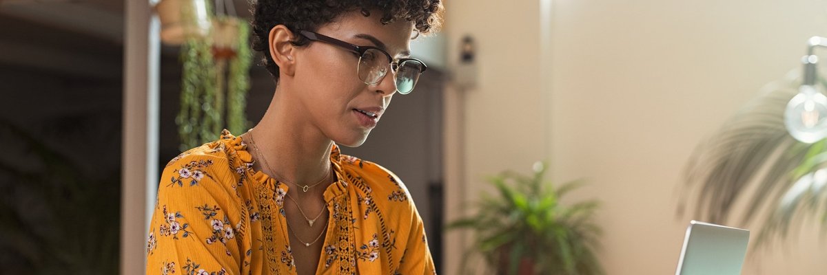 A female college student taking notes while studying on a laptop.