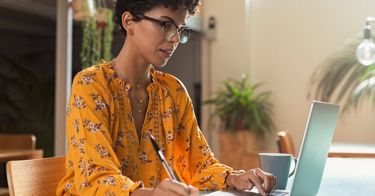 A female college student taking notes while studying on a laptop.