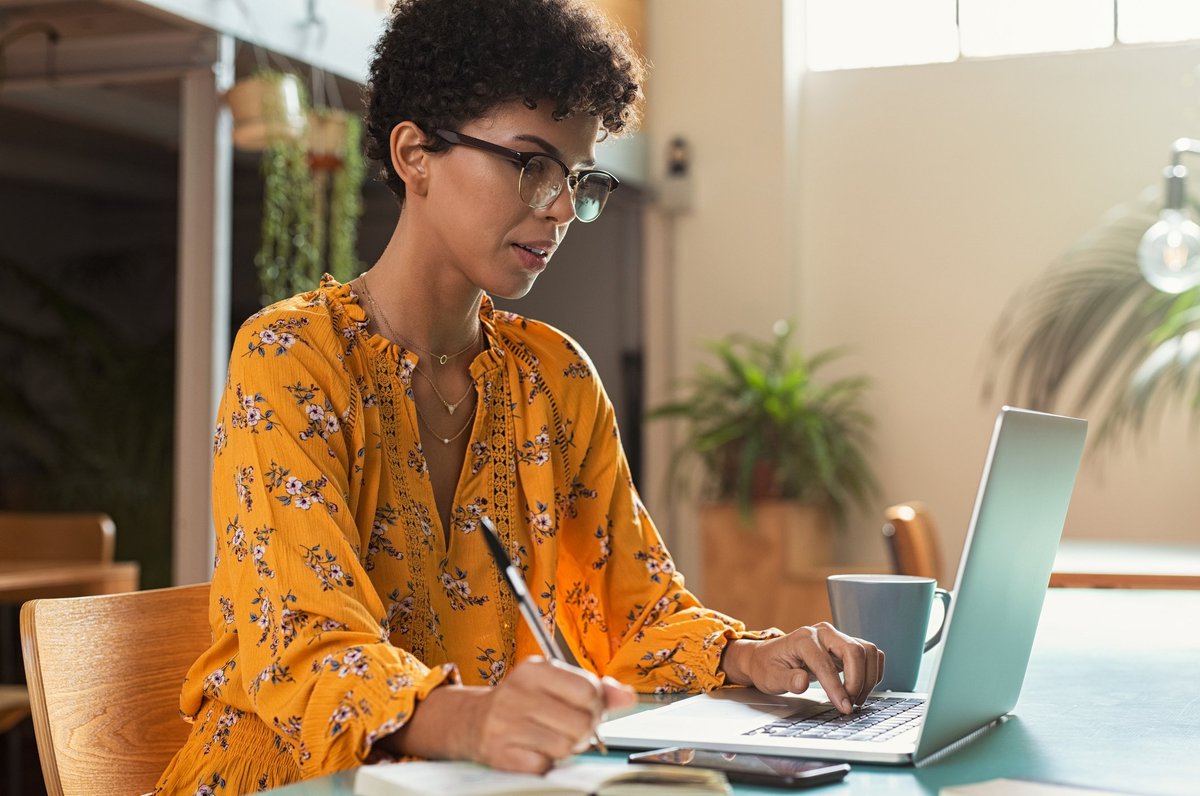 A female college student taking notes while studying on a laptop.