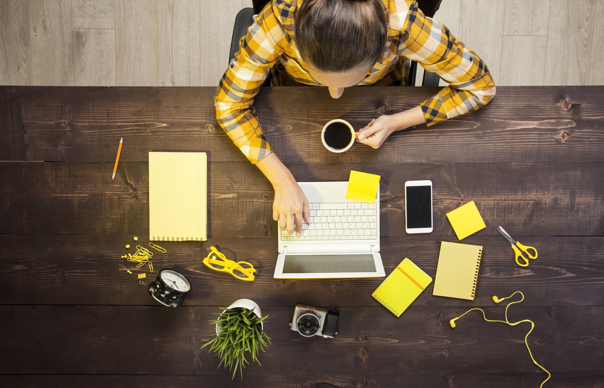A woman working on a laptop with notepads and other desk items around her.