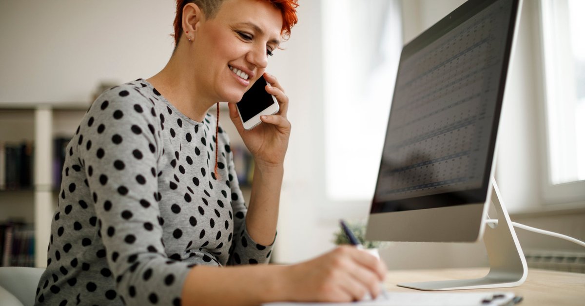 Woman working from home using computer, phone, and laptop.