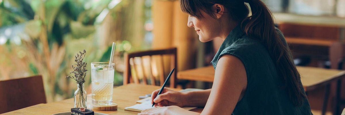Woman writes letter at cafe table.
