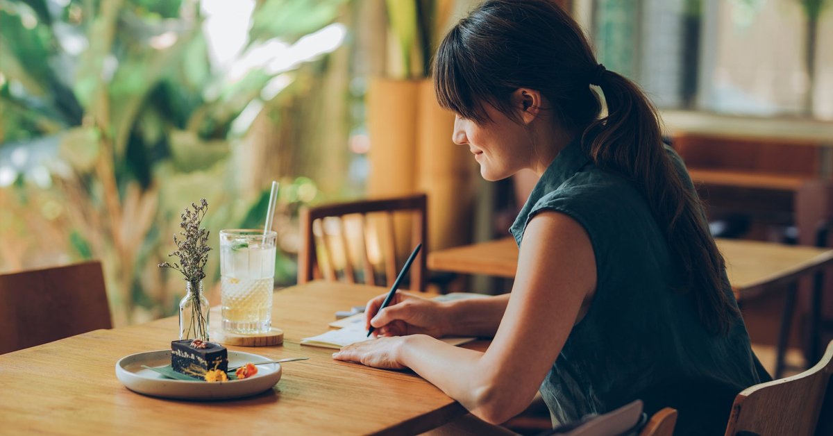 Woman writes letter at cafe table.