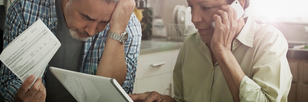 Worried looking mature couple with documents, phone, and laptop.
