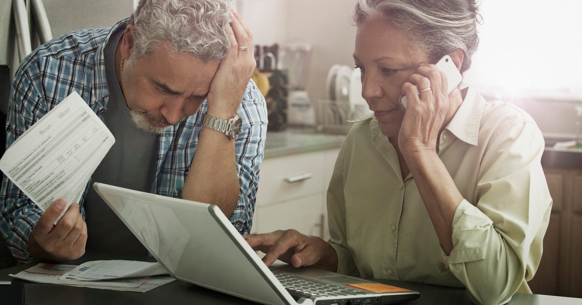 Worried looking mature couple with documents, phone, and laptop.