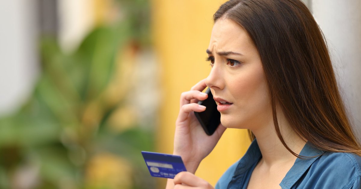 Worried-looking woman on phone holding at prepaid card.