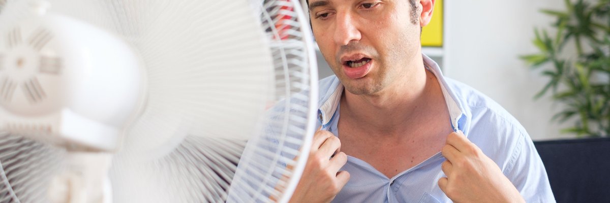 Man suffering from extreme heat sitting in front of fan.