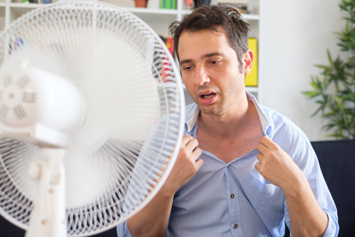 Man suffering from extreme heat sitting in front of fan.