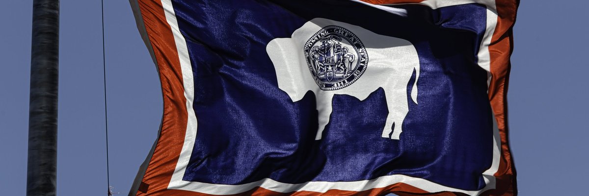 The state flag of Wyoming flying in front of a blue sky.