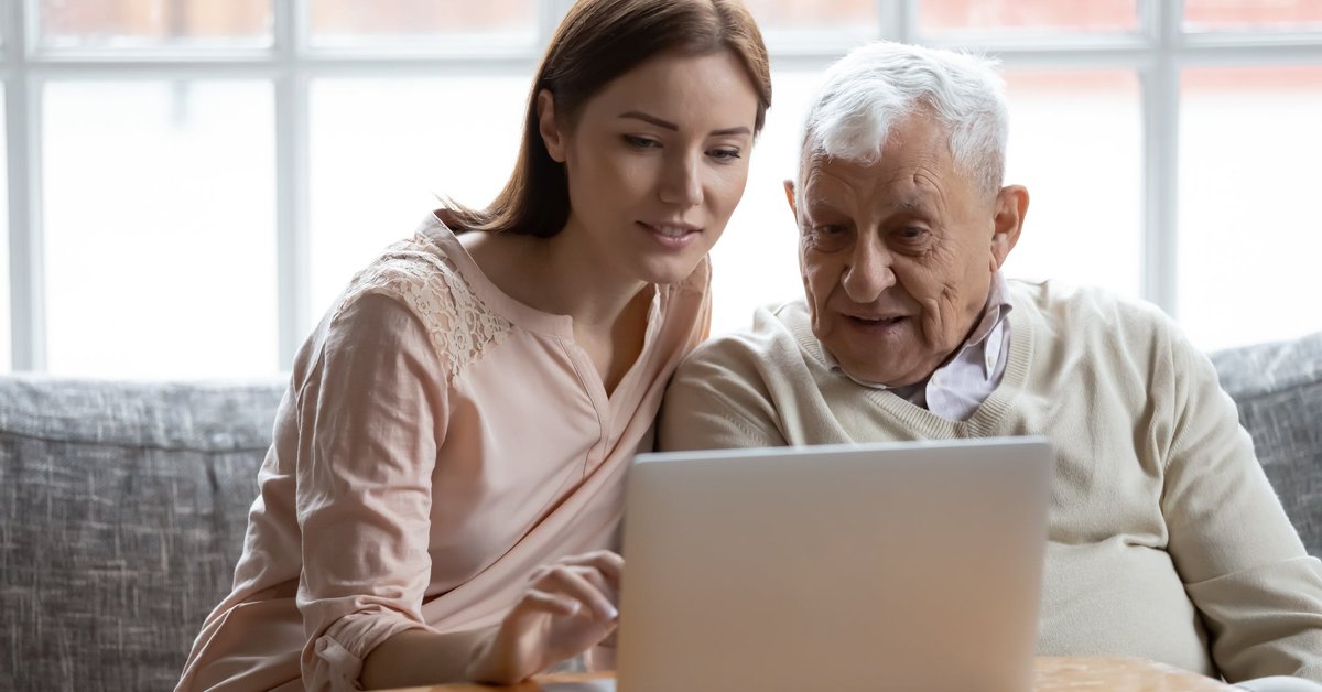 Young adult woman looking at laptop and talking with elderly man.