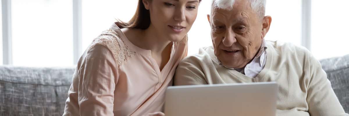 Young adult woman looking at laptop and talking with elderly man.