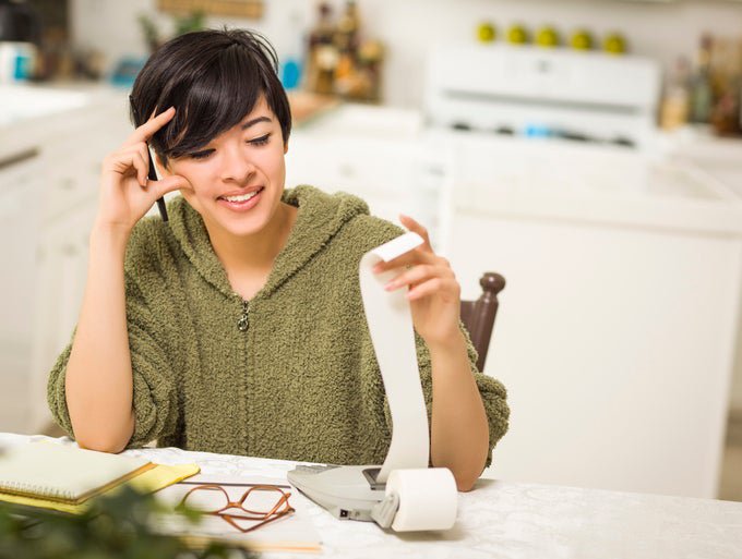 A young woman sitting at the kitchen counter smiles as she looks over her personal finance calculations.