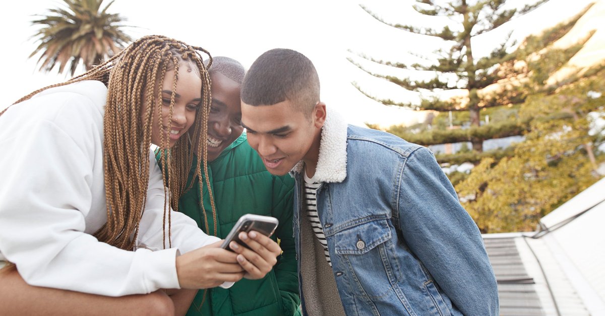Three young adults gathered looking at something on a cell phone screen.