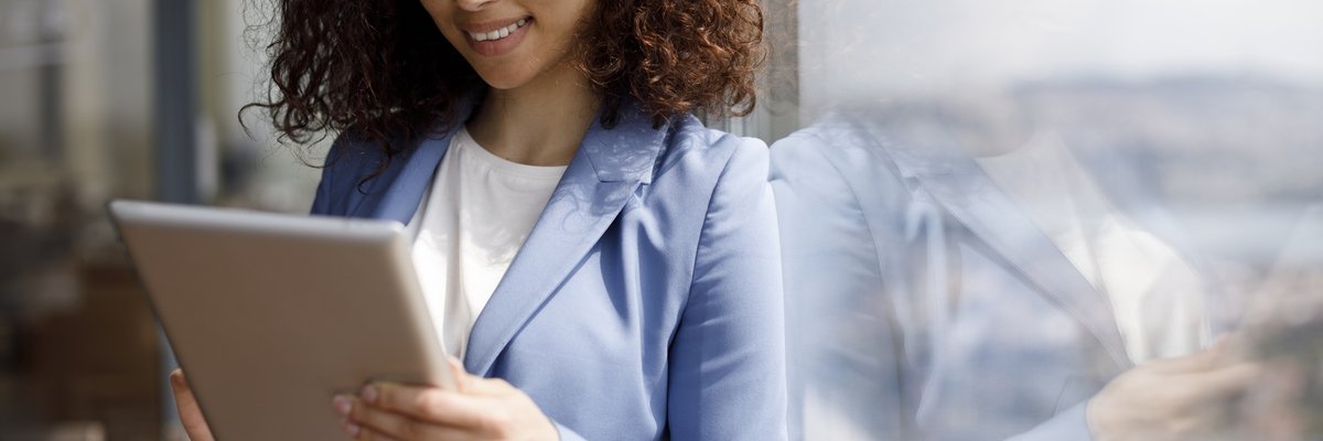 A young businesswoman leans against a window while looking at her tablet.