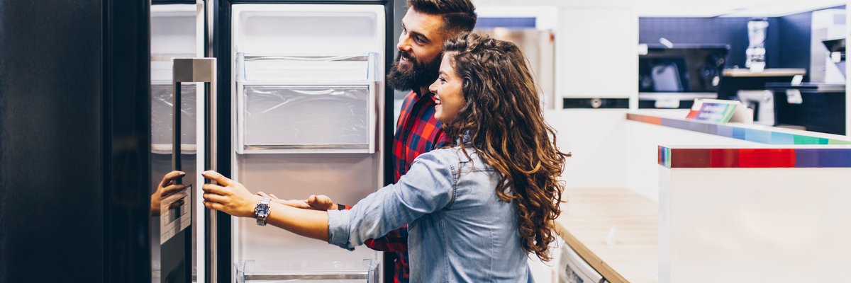 A young couple shopping for a new refrigerator at an appliance store.