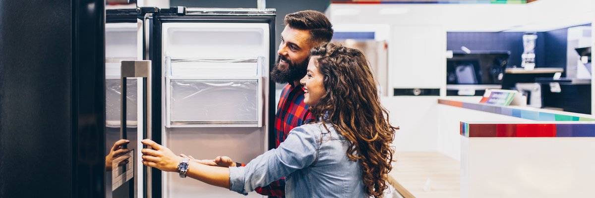 A young couple shopping for a new refrigerator at an appliance store.