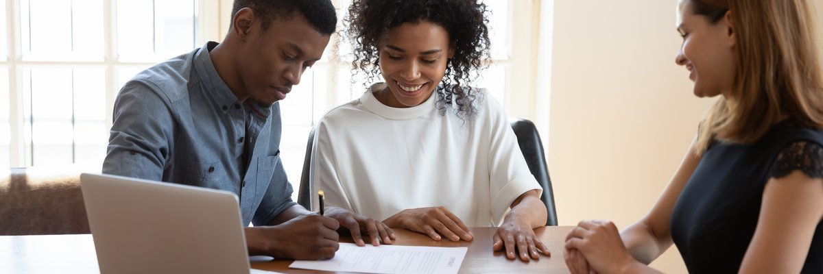 Young couple signing paperwork while a professionally dressed woman looks on.