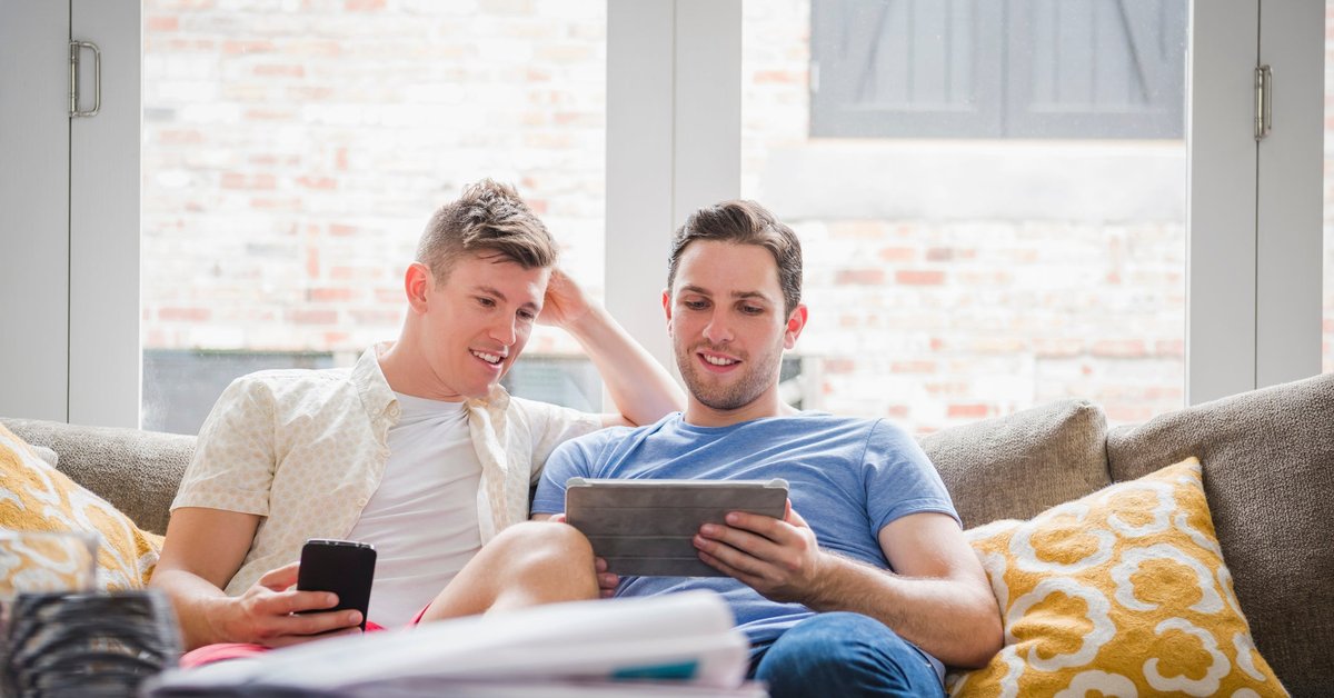 A young couple sit on a couch, looking at a tablet.