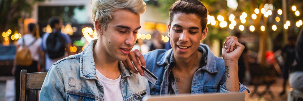 A young couple sit outside, looking at a computer. One is holding a credit card.