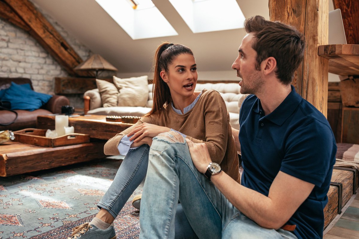 A young couple having a serious discussion sitting on their living room floor.