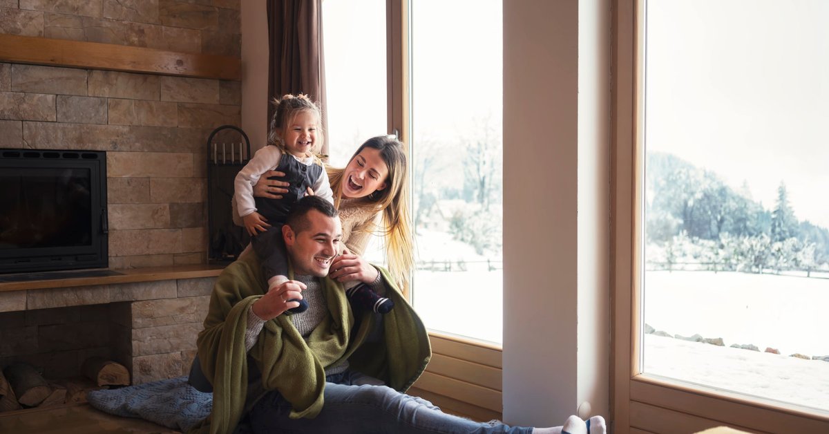 Young family bundled up in warm clothes by a window.