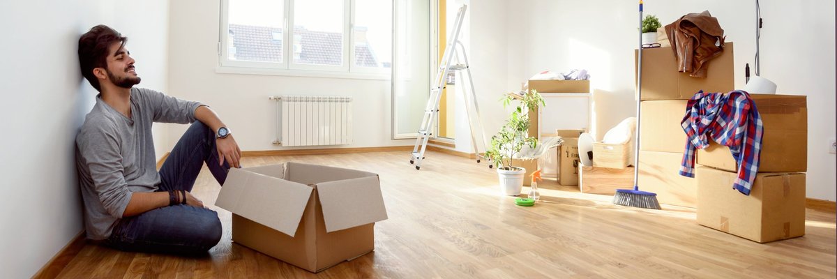 A smiling young man unpacking boxes on the floor of his new apartment.