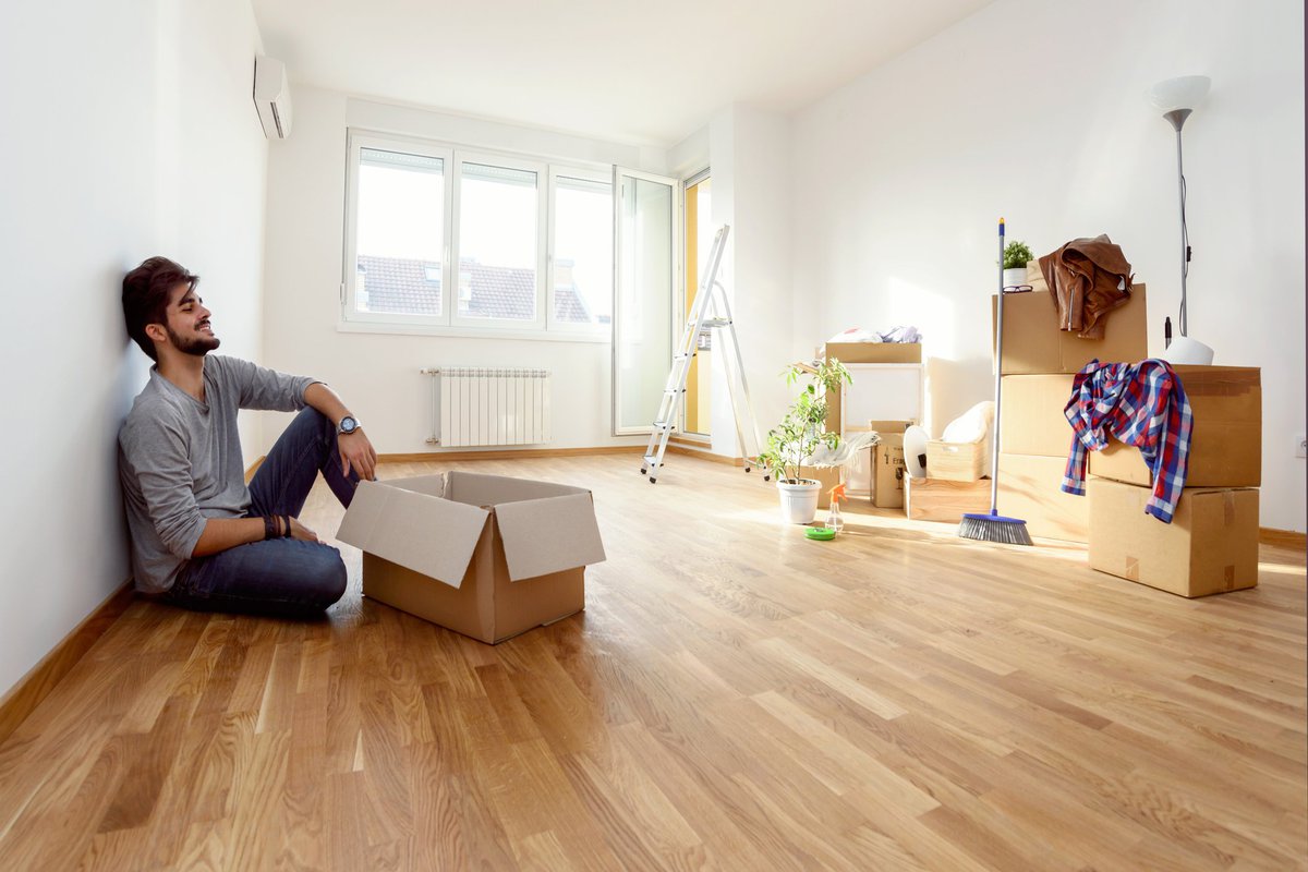 A smiling young man unpacking boxes on the floor of his new apartment.