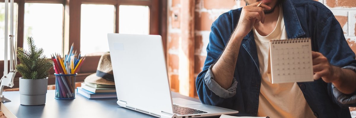 Young man pausing from using his laptop to look at a calendar.