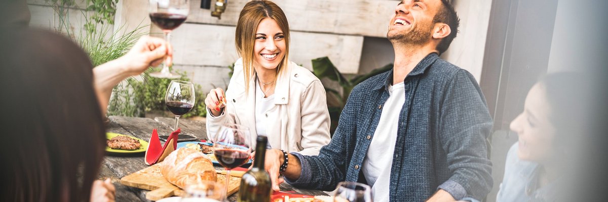 A group of smiling people having wine and food at a patio table.