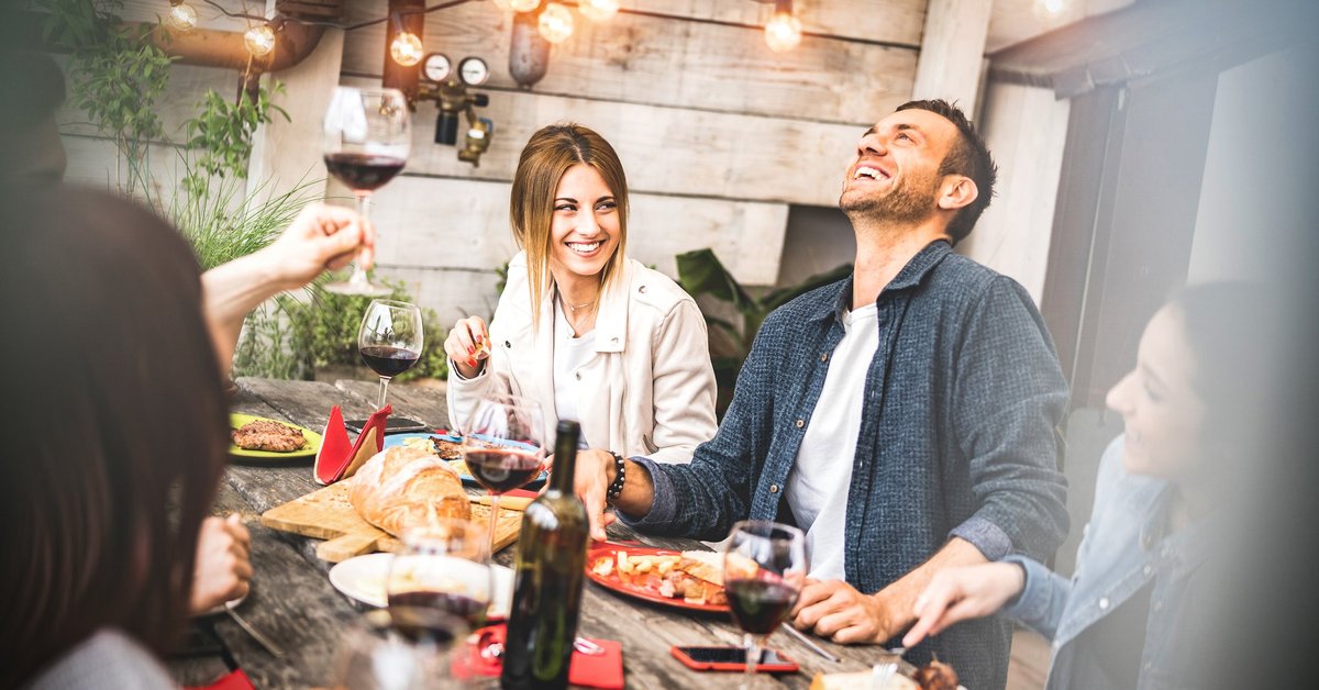 A group of smiling people having wine and food at a patio table.