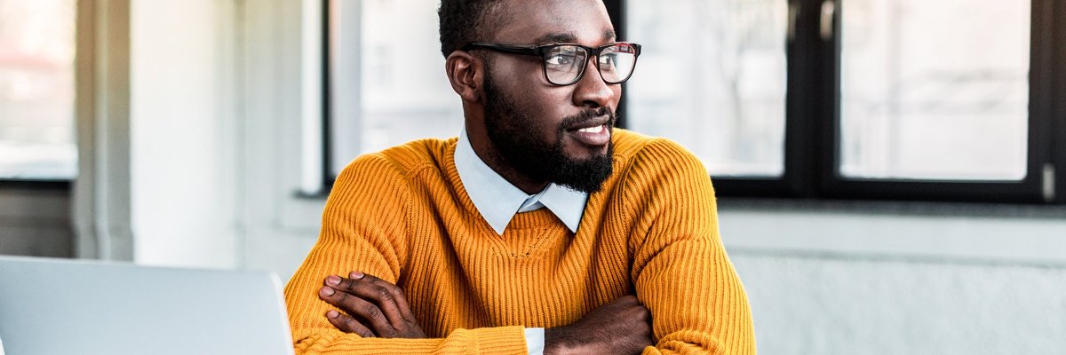 A smiling young professional man sitting in front of an open notebook and laptop.
