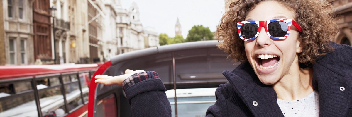 Young traveler on a trolley in London wearing sunglasses with British flag design on them.