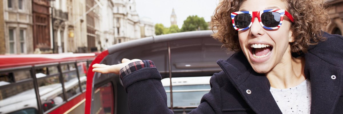 Young male traveler on a trolley in London wearing sunglasses with British flag design on them.