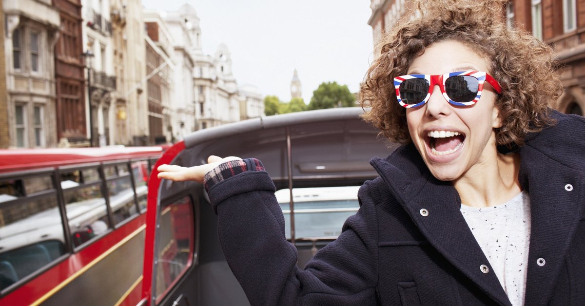Young male traveler on a trolley in London wearing sunglasses with British flag design on them.