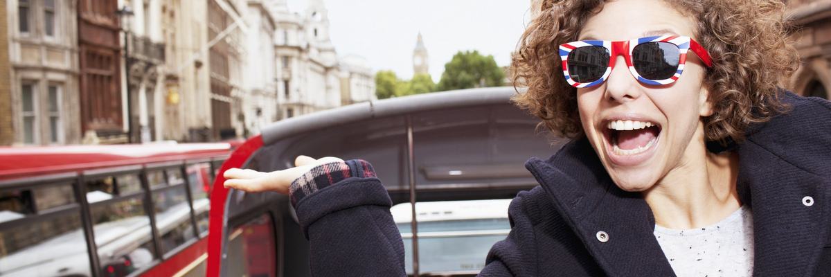 Young male traveler on a trolley in London wearing sunglasses with British flag design on them.