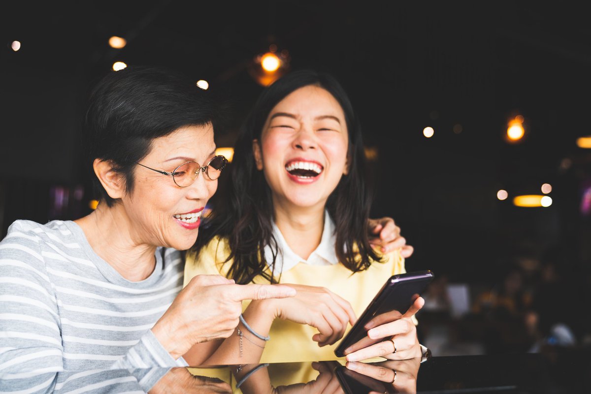 A young woman and her mother looking at a phone and laughing.