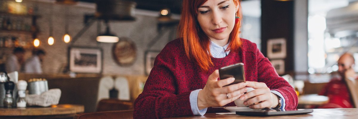 A young woman at a coffee shop looking at her phone.