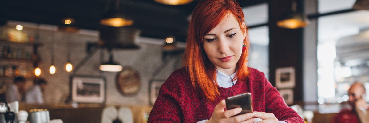 A young woman at a coffee shop looking at her phone.