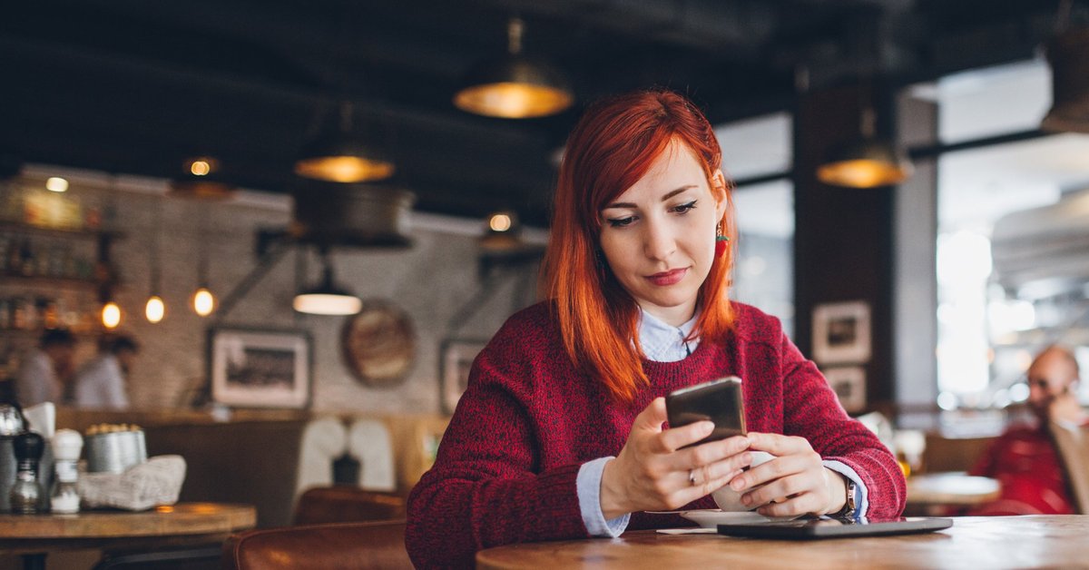 A young woman at a coffee shop looking at her phone.