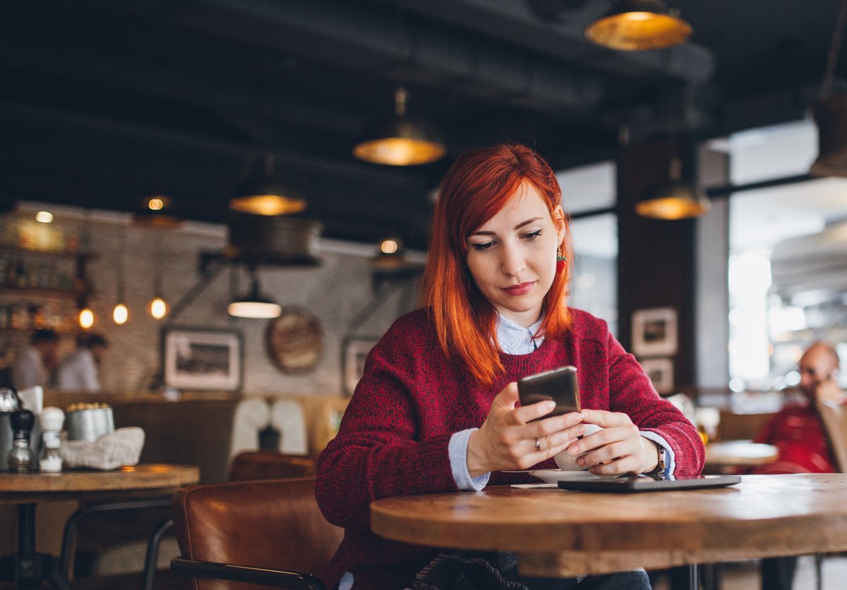 A young woman at a coffee shop looking at her phone.