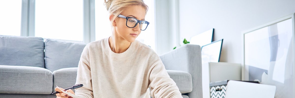 A young woman sitting on the floor with a calculator, laptop, and notebook.
