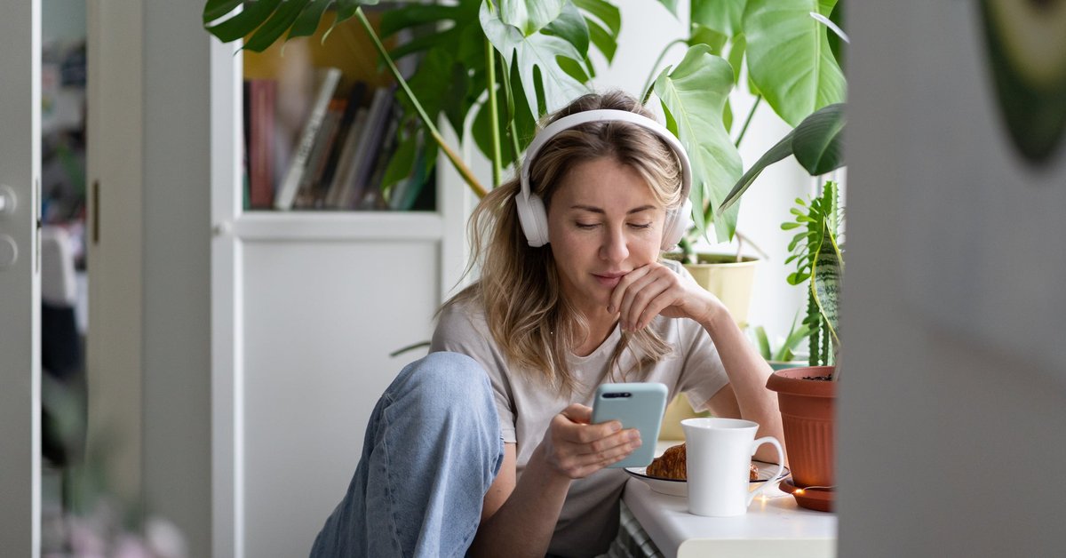 Young woman listening to podcast on her headphones while drinking coffee.