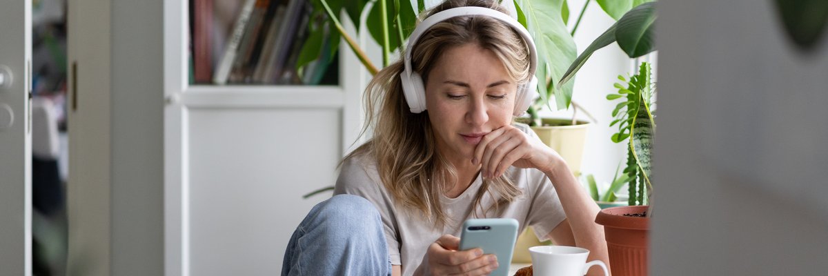 Young woman listening to podcast on her headphones while drinking coffee.